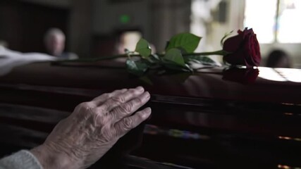 Coffin, flower and hands of person at funeral for goodbye with grief, loss or pain of mourning closeup. Sad, death and rose for respect with widow in church for farewell ceremony or memorial service