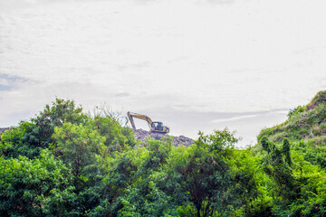 View of an excavator on a pile of rubbish from a distance, an overloaded landfill in Slamaran Pekalongan, Central Java