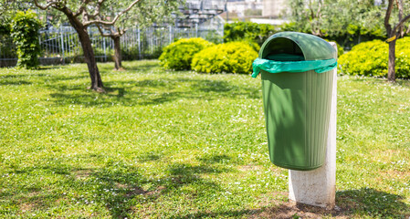 Green park trash bin in spring sunlight, banner with copy space. Clean environment, urban maintenance, and public cleanliness awareness.