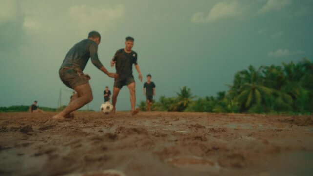 Two young men fall in muddy field during intense football in the rain, slow motion