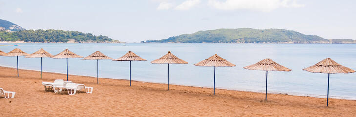 Empty beach with straw umbrellas and lounge chairs, banner. Coastal relaxation, vacation ambiance and summer leisure by the sea.