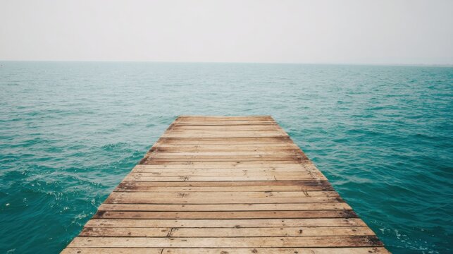 Weather-worn wooden dock extending into serene turquoise water with gentle ripples, aged planks showing discoloration, calm overcast sky meeting the horizon, emphasizing solitude and tranquility.