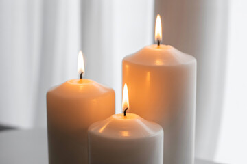 Three white candles with burning flames on a soft background