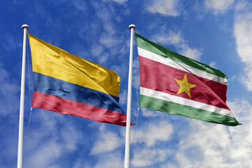 Waving flags of Colombia and Suriname against a vibrant blue sky, symbolizing international relations and friendship.