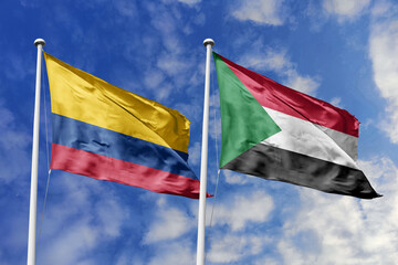 Waving flags of Colombia and Sudan against a vibrant blue sky, symbolizing international relations and friendship.