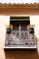 Wrought iron balcony with potted plants and wooden blind in Villanueva de los Infantes town