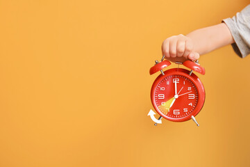 Child's hand with alarm clock on color background