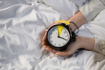Woman with alarm clock in bedroom, top view. Spring forward concept