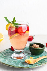 Glass of infused water with strawberry and lemon on light background