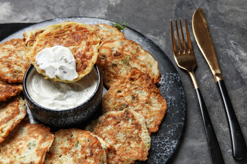 Board of tasty zucchini fritters with sour cream on dark background