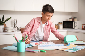 Little boy with pencil case drawing at table in kitchen