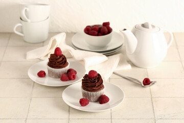 Plates of tasty chocolate cupcakes with raspberries and teapot on table