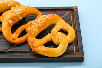 Wooden board with soft pretzels on blue background