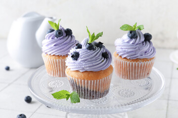 Glass stand of delicious cupcakes with blueberries and mint on white tile table