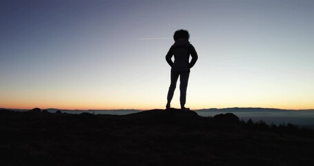 Silhouette of a Woman Hiker Standing on a Mountain Peak at Sunset