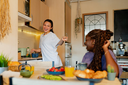 Two joyful female roommates are preparing and enjoying a healthy breakfast in their modern kitchen - Powered by Adobe