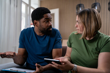 Worried interracial couple facing financial stress at home, struggling with rent, housing costs,...