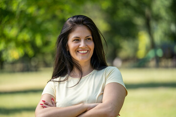 Smiling mature fitness woman with beautiful hair and crossed arms posing confidently outdoors in nature, healthy lifestyle and natural beauty concept