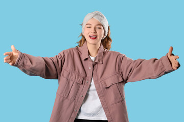 Smiling young woman in headband opening arms for hug on blue background