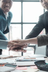 Business team in office and shaking hands after signing contract. Business colleagues clasp hands around desk with laptop and data chart in office.