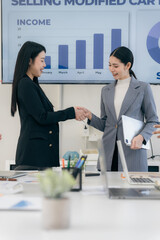 Business team in office and shaking hands after signing contract. Business colleagues clasp hands around desk with laptop and data chart in office.