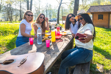 Cheerful young women taking selfie at picnic table in a park during a sunny day