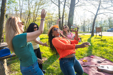 Four cheerful women dancing and filming in a park