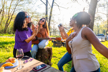 Multi ethnic friends singing and playing guitar at picnic in a park