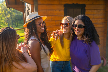 Four cheerful women laughing and embracing outdoors near a wooden house