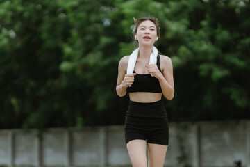 A fit and focused woman jogs outdoors in a serene green park, wearing activewear and earphones,...