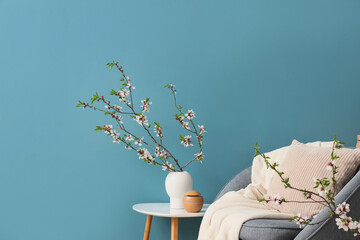 Grey armchair and vase with blooming branches on coffee table near blue wall
