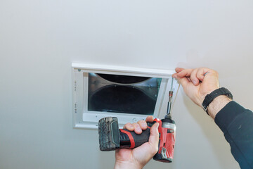 Worker using drill to secure ceiling vent in contemporary room during home improvement