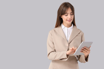 Fototapeta premium Beautiful young businesswoman with modern tablet computer on grey background