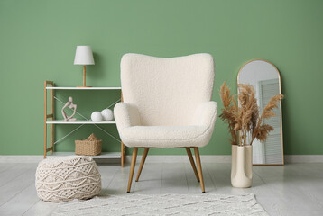 Stylish living room with white armchair, mirror and vase of pampas grass