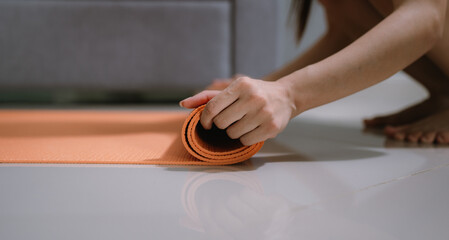 A woman practices yoga indoors on a mat, sitting in a relaxed pose. She smiles peacefully,...