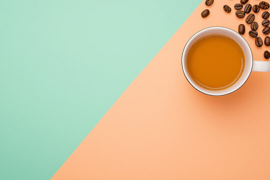 A cup of coffee with scattered beans sits on diagonally split orange and mint green background.