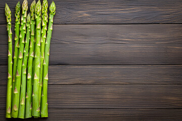 Fresh green asparagus spears are arranged neatly on a dark rustic wooden surface background.