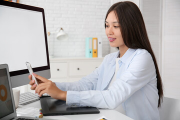 Female Asian graphic designer with mobile phone taking selfie in office
