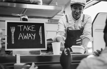 People are waiting outside of food truck while young chef preparing dinner - Summer meal and small business concept concept - Focus on man worker face - Black and white editing