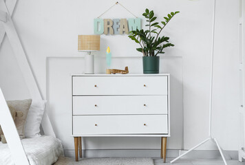 Chest of drawers with toy plane, lamp and houseplant in light nursery