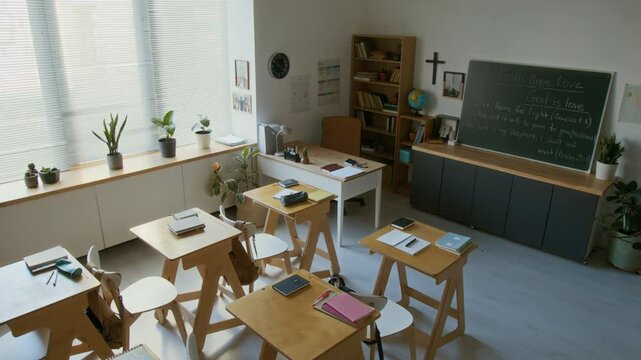 No people high angle shot of empty classroom in modern Christian school with crucifix on wall, Bible quotes on blackboard and holy books on desks