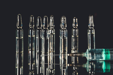 Ampoules and syringe against a dark background. Pharmaceutical concept for vaccination, medication, and healthcare.