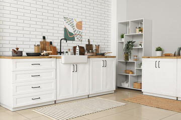 Shelving unit and kitchen counters with utensils near white brick wall