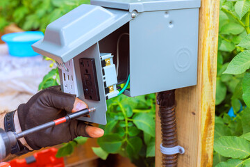 Electrician worker is installing USB ports an outdoor electrical outlet box while tending to backyard garden