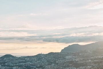 Panoramic view of a city on a hillside overlooking the ocean at sunrise or sunset with cloudy sky