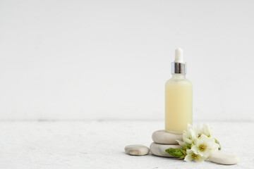 Bottle of essential oil, spa stones and flower on light background