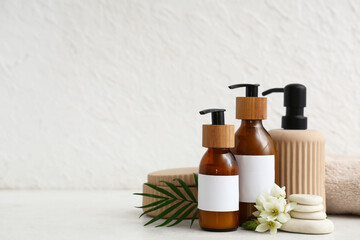 Bottles of cosmetic products, spa stones, towel and flowers on light background