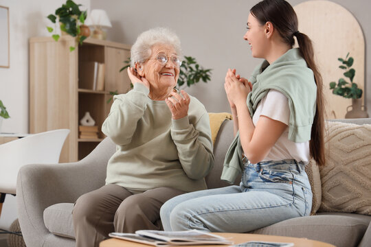 Senior woman with hearing aid and her granddaughter sitting on sofa at home