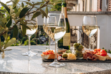Outdoor dining or aperitif white wine glasses on a stone table with gourmet charcuterie board assorted meats, olives, and cheese