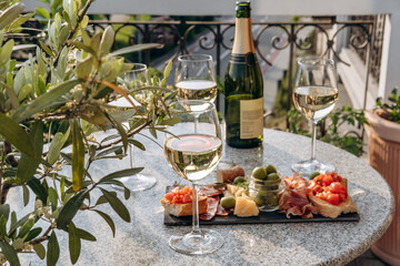 Outdoor dining or aperitif white wine glasses on a stone table with gourmet charcuterie board...